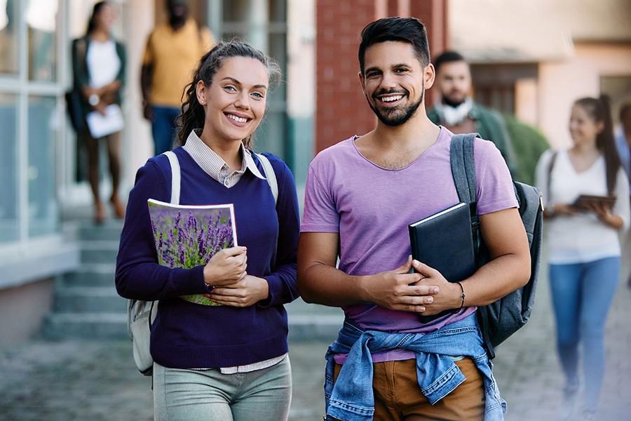 2 college students smiling. One student is wearing a lavender color t-shirt and the other student is holding a notebook that has a field of lavender pictured on the back of it.